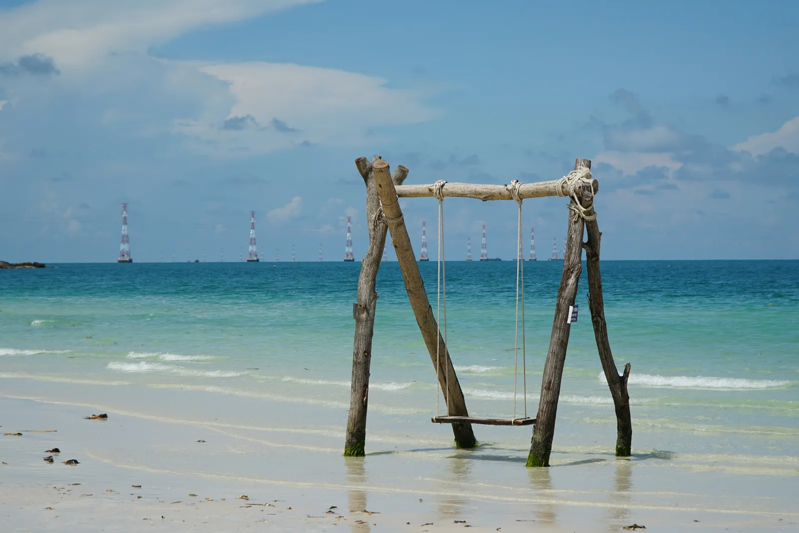 A wooden swing on a Phu Quoc beach, with a line of pylons across the sea on the horizon