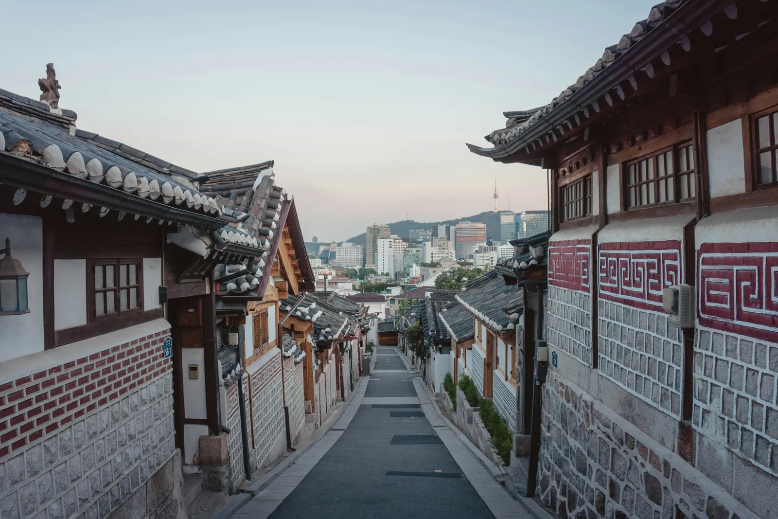 A hanok lane in late-afternoon light, with central Seoul behind