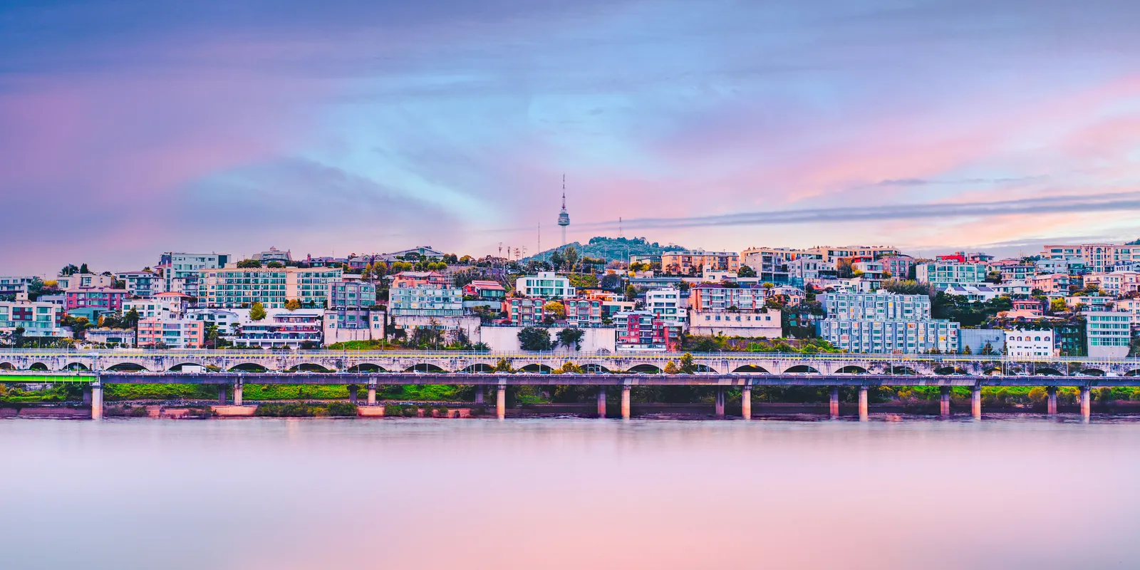 A city skyline and bridge across the river at dusk